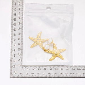 Detailed view of starfish earring with gold plating, zircons and white pearl on scale