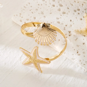 Detailed view of a gold ocean-themed open bangle with a starfish and shell on travertine