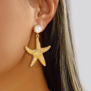 Close-up of model wearing gold starfish earrings with white pearls and sparkling crystals