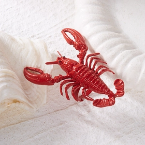 Macro detail of glossy red lobster-shaped jewelry set resting inside a white seashell