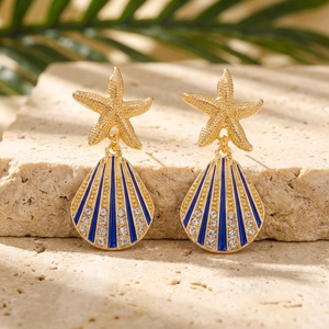 Dettaglio macro di orecchini a stella marina e conchiglia con smalto blu e cristalli