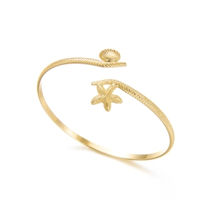 Detail of golden starfish and seashell charms on textured woven metal arm cuff bracelet