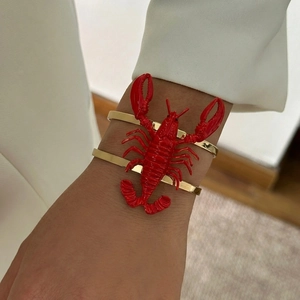 Detailed close-up of a gold multi-layer bracelet with a 3D red lobster accent on the wrist