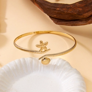 Detailed close-up of gold starfish and scallop shell arm cuff with textured band