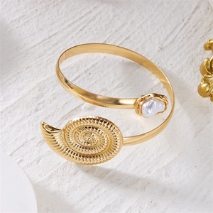 Detailed close-up of golden shell arm cuff with a baroque pearl on a stone surface