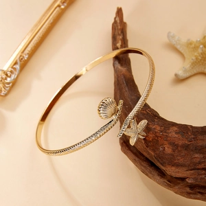 Detailed close-up of golden starfish and seashell cuff bracelet on a rustic wood branch