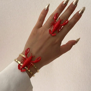Detailed view of the oversized 3D red lobster ring and golden bangle set on model hand