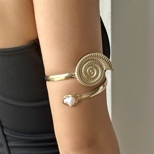 Detailed close-up of golden spiral arm cuff with seashell design and white pearl inlay