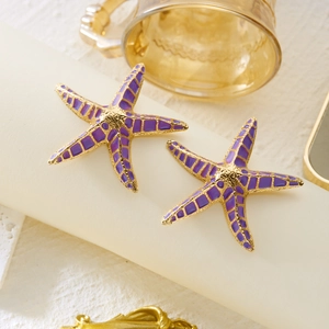Detail of purple enamel starfish earrings with golden base on a minimalist pedestal