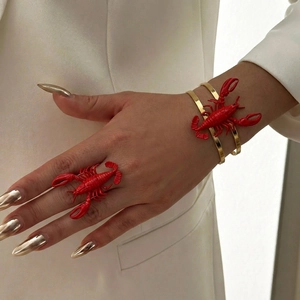 Detail of red lobster enamel jewelry set with ring and cuff worn on model hand