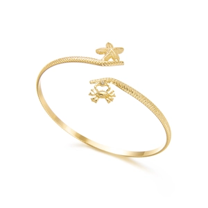 Macro shot of gold starfish and crab charm details on a wave textured arm cuff