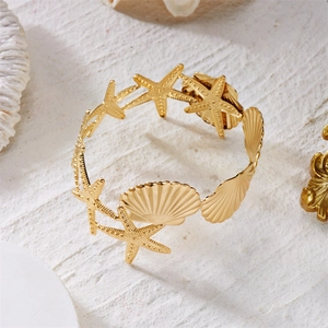 Detail of golden sea star and shell arm bracelet on white coral beach background