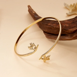 Detail of a gold crab and starfish open bangle with textured band on a beach themed background