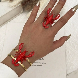 Detailed view of creative red lobster ring and gold-tone cuff bracelet worn on model's hand