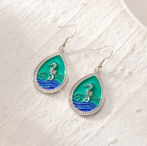 Detailed close-up of teardrop hook earrings with silver seahorse and green enamel inlay