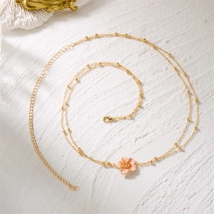 Vue détaillée de la chaîne de taille dorée avec fleur en émail rose et perles sur pierre