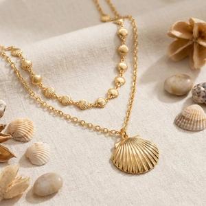 Double-layered golden ocean shell and scallop pendant necklace on a natural linen background