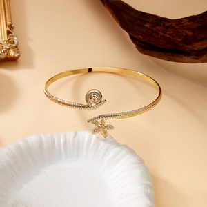 Detailed view of golden starfish and seashell open arm cuff on a ceramic plate