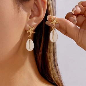 Bohemian gold starfish and white cowrie shell dangle earrings worn by model