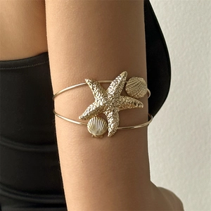 Detail of a golden starfish arm cuff with seashell accents on a model arm