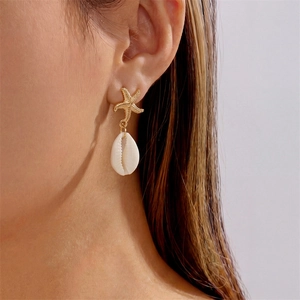 Close-up of starfish and seashell drop earring worn by a model in soft light