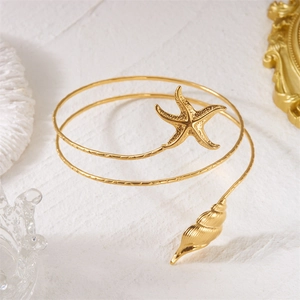 Detailed shot of golden arm cuff featuring textured starfish and conch seashell charms