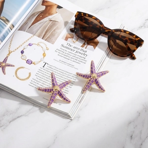 Detail view of purple starfish earrings with gold enamel on a fashion magazine