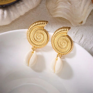 Detailed shot of golden sea shell earrings with natural cowrie shell on a ceramic bowl