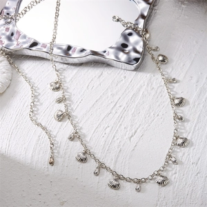 Gros plan d'une chaîne de taille argentée avec pendentifs coquillages sur fond texturé