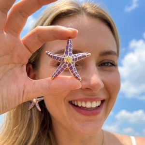 Detail of purple enamel starfish earrings with gold grid pattern on model ear