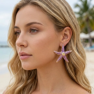 Close-up of a model wearing large purple starfish enamel earrings with gold accents
