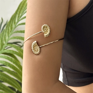 Detail of bohemian gold armlet featuring textured seashell and conch on upper arm