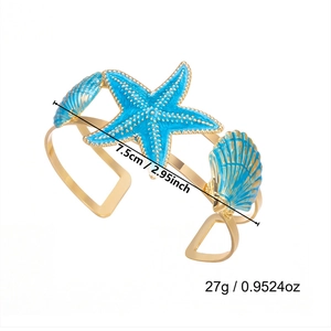 Detail view of starfish and seashell ornaments on a gold arm cuff with dimensions