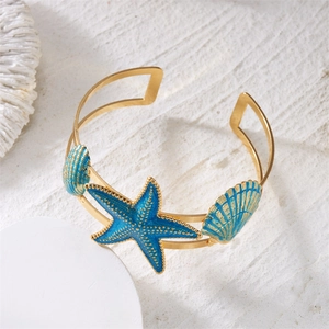 Detailed shot of bohemian gold arm cuff with blue starfish and seashells on white sand