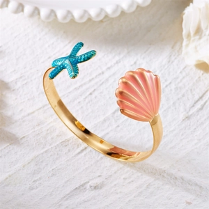 Detail of golden seashell and blue starfish arm cuff on white stone surface
