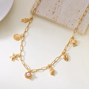 Detail of gold shell necklace with starfish, turtle pendants and white pearl on travertine