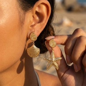 Detailed view of asymmetric golden starfish and seashell earrings worn on a beach setting