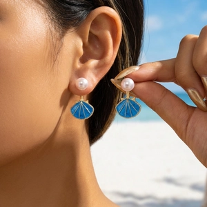 Dettaglio degli orecchini a conchiglia in smalto blu e perla sulla spiaggia