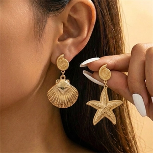 Close-up of asymmetric gold starfish and seashell earrings with brushed metal texture