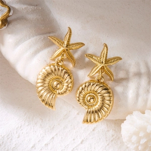 Close-up of gold starfish and seashell drop earrings on a white coral background