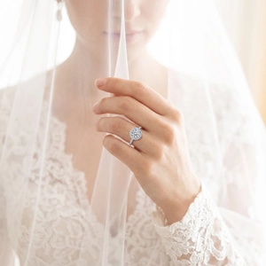 Elegant four-prong halo engagement ring worn by a bride with lace wedding dress