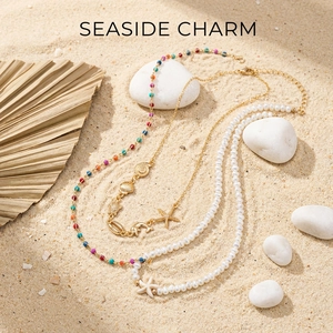 Detail of seashell pendants and pearl bead necklaces on a sandy summer beach background