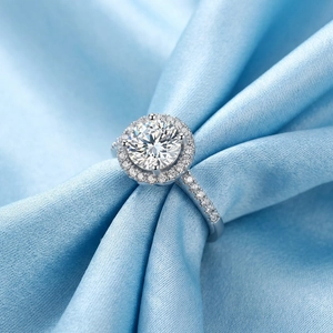 Elegant halo four-prong silver ring with large round solitaire and pave diamonds on blue silk