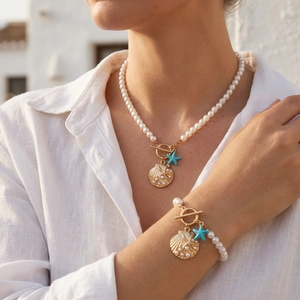 Detail of bohemian pearl jewelry set with starfish pendants on woman's neck and wrist