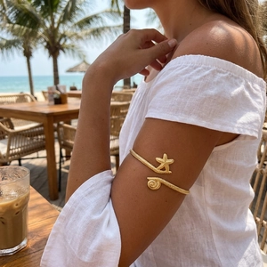 Bohemian gold starfish and seashell arm cuff with woven texture on a vacation beach