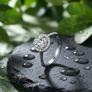 Close-up of a halo diamond ring with a round center stone on black slate and green leaves