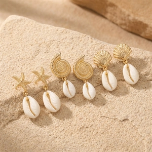Three pairs of gold starfish, conch, and shell earrings with white natural cowrie drops