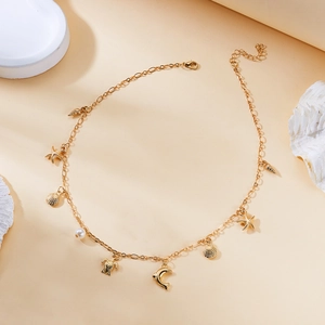 Detail of gold layered necklace with starfish and turtle charms on sand background