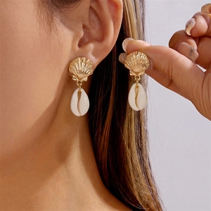 Golden scallop and white cowrie shell drop earrings shown on a model for beach fashion