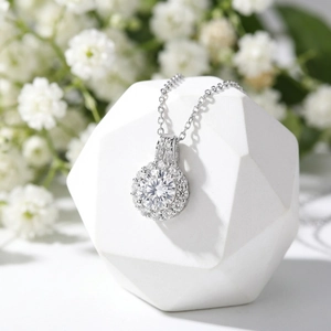 Close-up of a silver four-prong round moissanite pendant with halo setting on a display stone